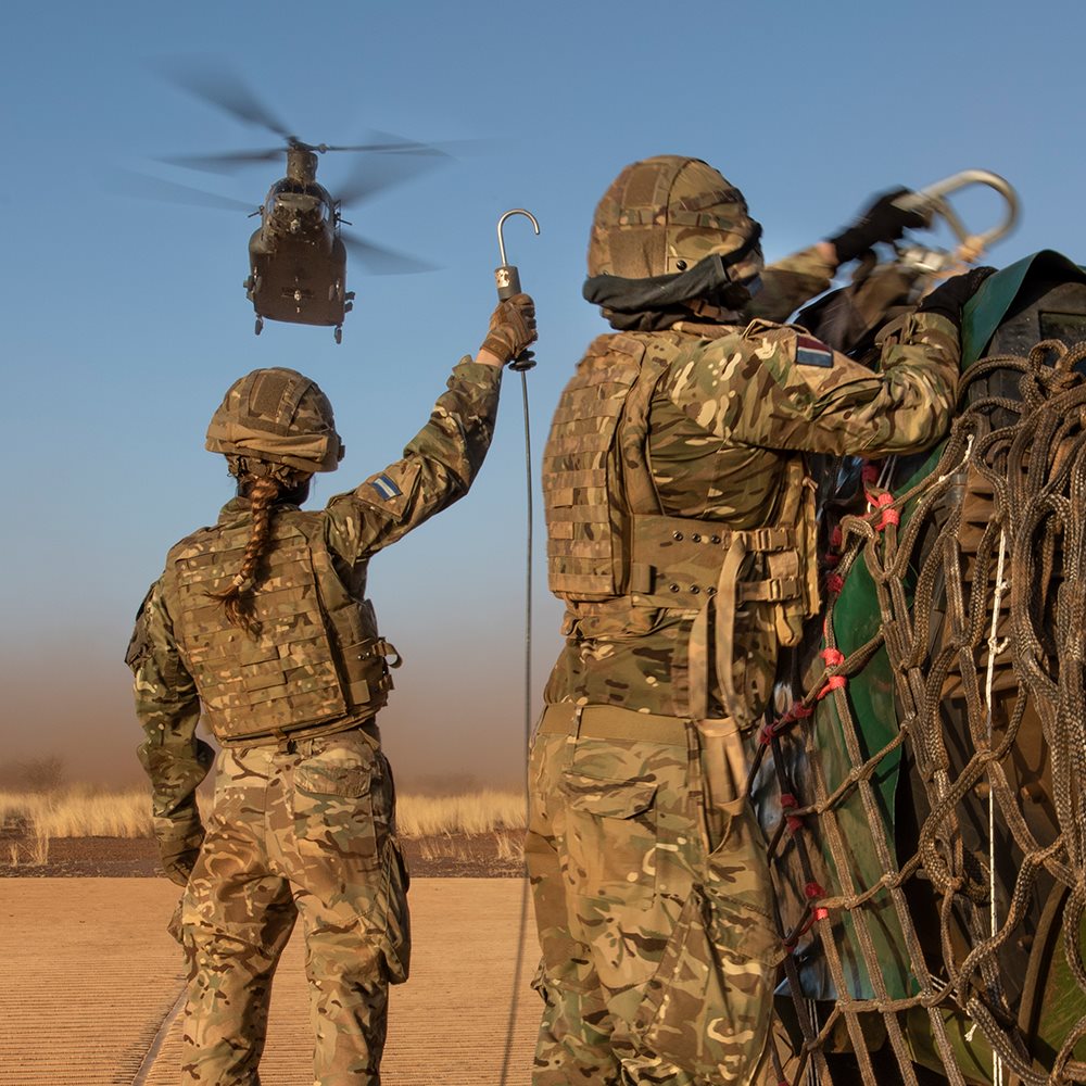 Two servicewomen in the desert with a helicopter in the background